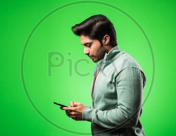 Indian / Asian man with smartphone, standing isolated over green background