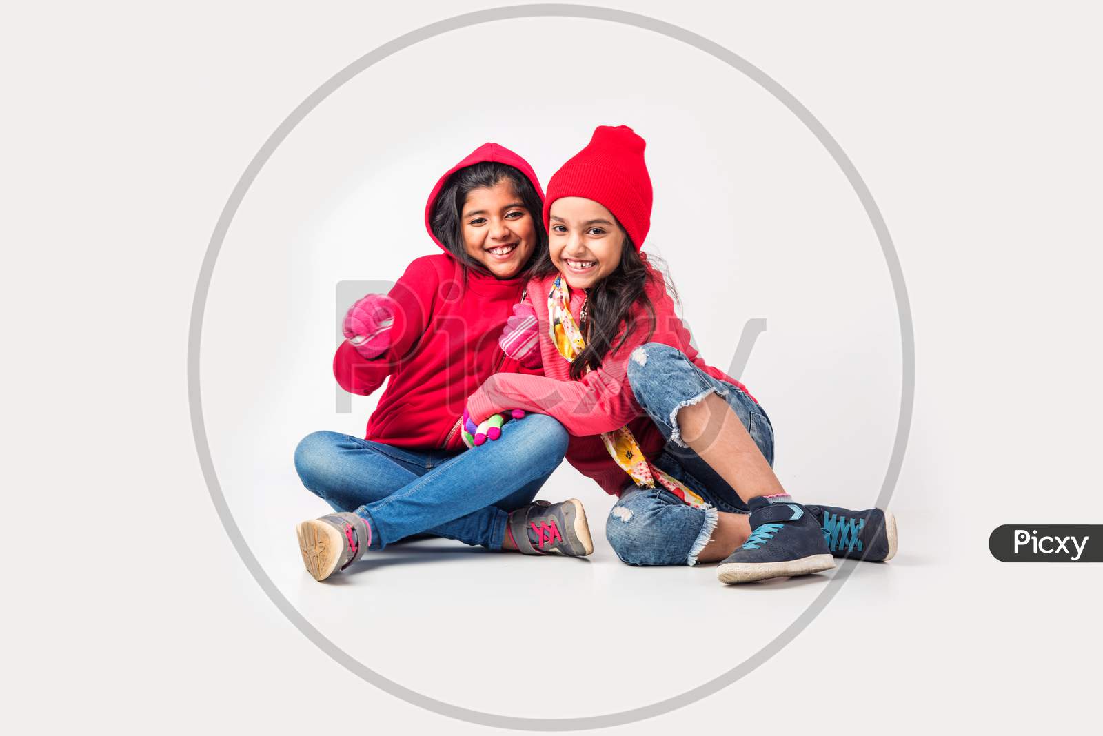 Two Indian little girls in warm cloths sitting and playing against white background