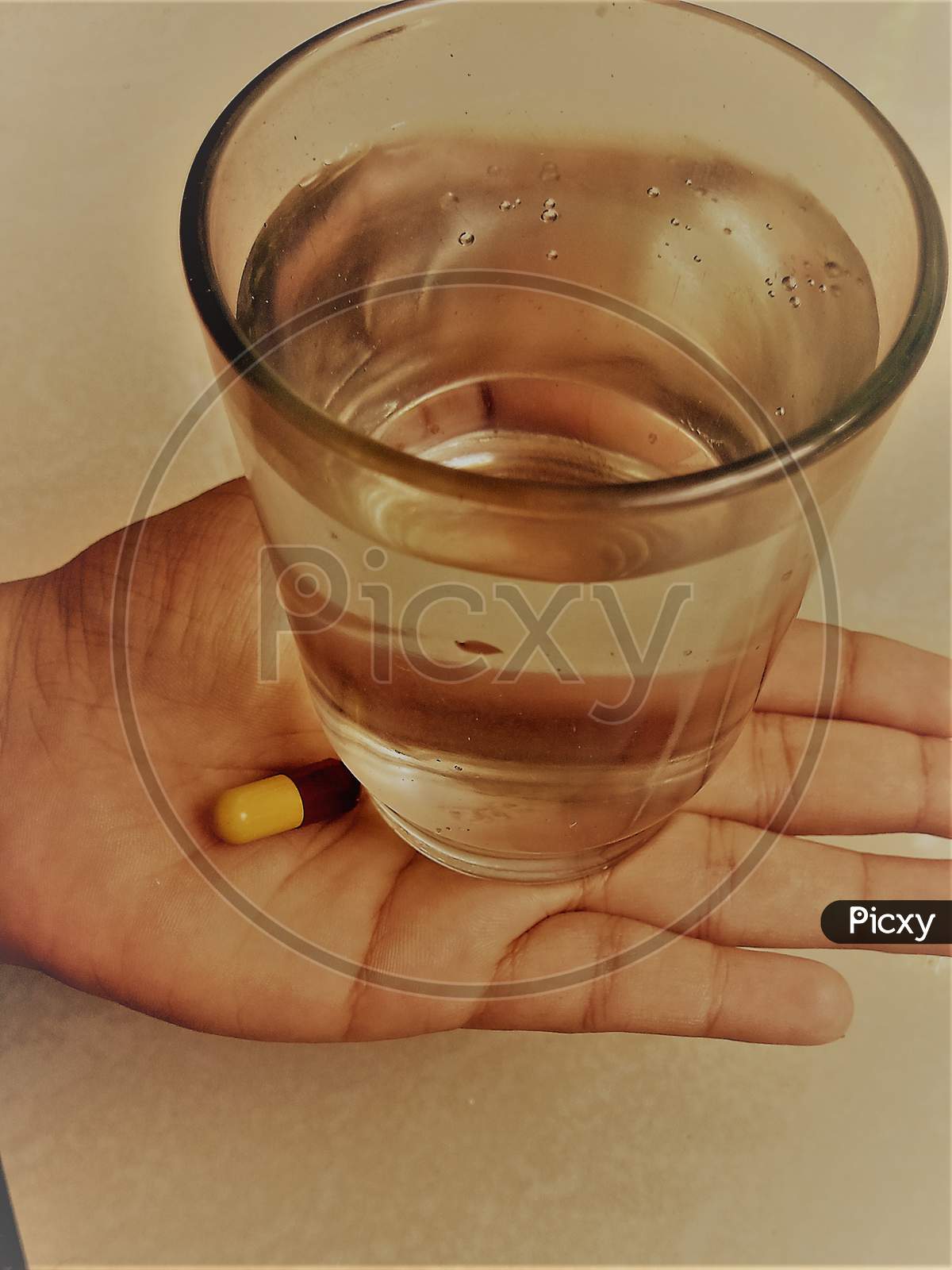 A Glass of water and a tablet placed near to it on a hand.