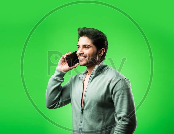 Indian / Asian man with smartphone, standing isolated over green background