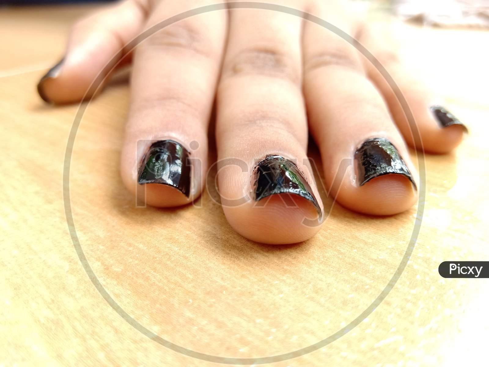 A Closeup Of Black Nail Polished Hand On Table.