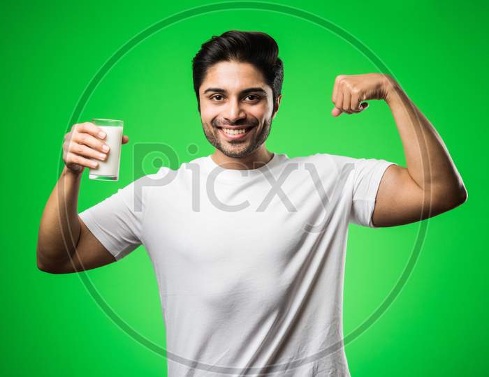 Indian man drinking milk in glass while standing isolated over green background
