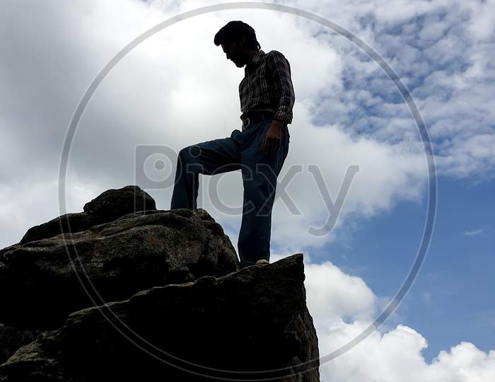 Portrait of a young handsome Indian guy standing on cliff in the height of a mountain in hilly area of Himachal Pradesh, India