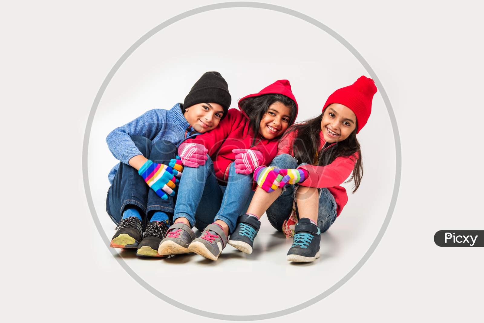 Three Indian /asian kids in winter wear sitting against white background and having fun