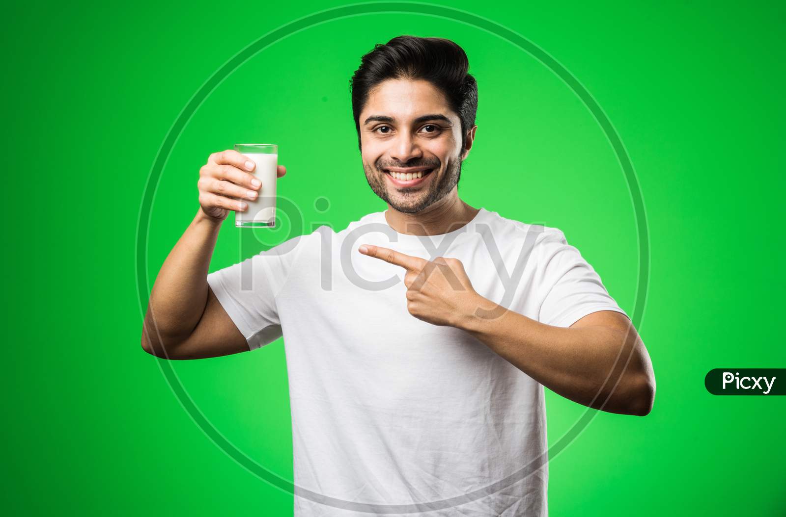Indian man drinking milk in glass while standing isolated over green background
