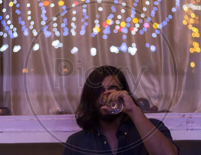 Young Man Drinking Red Wine At Home With Colorful Lights In The Ceiling.X