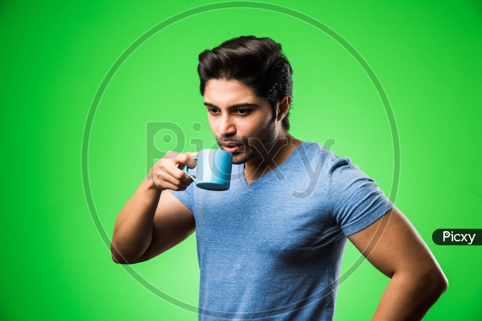 Indian man with tea / coffee cup or mug. Drinking, presenting or holding while standing isolated over green background