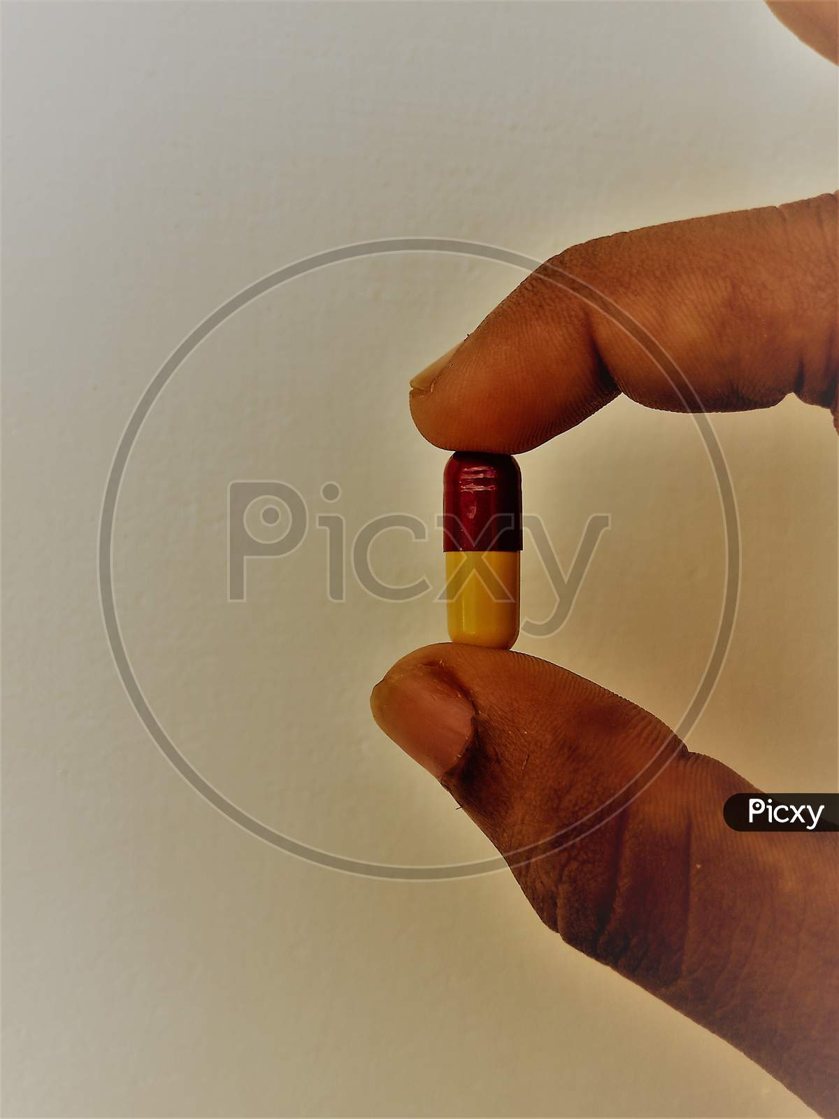 A tablet is been hold using thumb and forefinger in a white background.