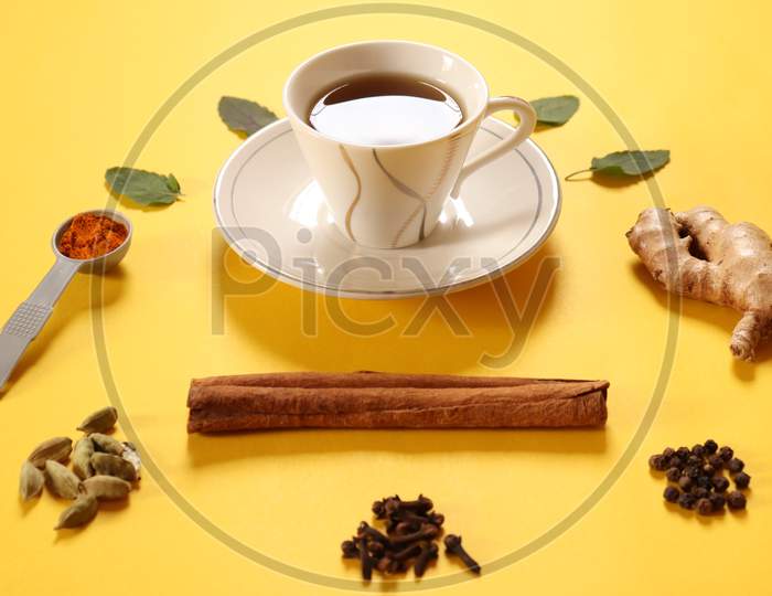 Refreshing green tea, herbal tea with ingredients ginger, cinnamon, turmeric, tulsi, cloves, cardamom and black pepper to boost immunity during COVID 19 or coronavirus on yellow background.