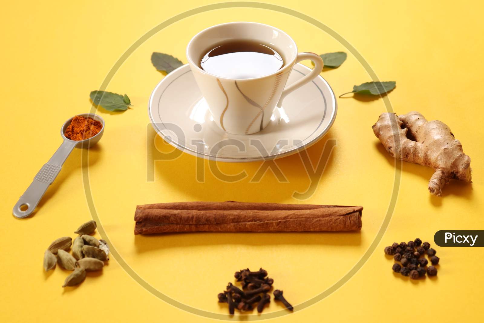 Refreshing green tea, herbal tea with ingredients ginger, cinnamon, turmeric, tulsi, cloves, cardamom and black pepper to boost immunity during COVID 19 or coronavirus on yellow background.