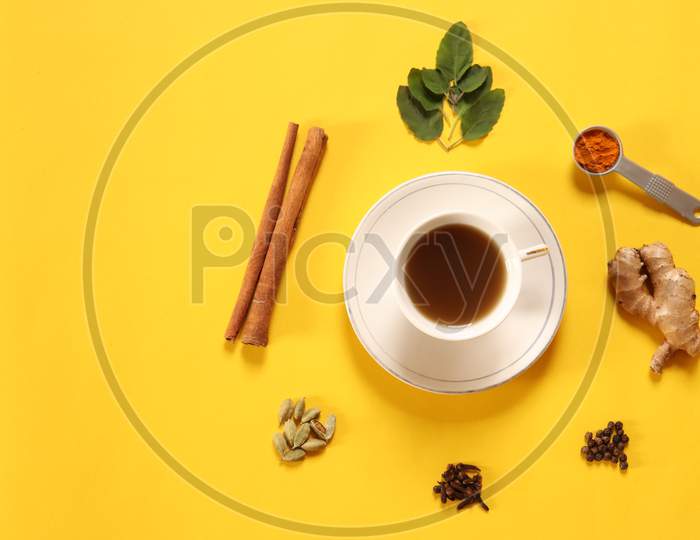Flat lay of refreshing green tea, herbal tea with ingredients ginger, cinnamon, turmeric, tulsi, cloves, cardamom and black pepper to boost immunity during COVID 19 or coronavirus on yellow background