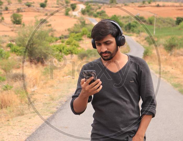 Young Indian Man using a Smartphone or Mobile Phone with Headphones on