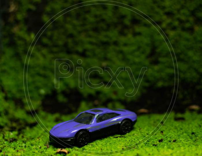 A Toy Car In A Green Grass Surface With Beautiful Blurry Background