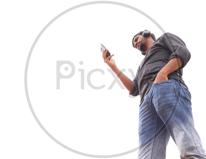 A Young Indian Man using a Smartphone or Mobile Phone with Headphones on