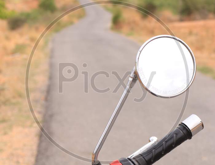 Selective on Royal Enfield Bike Mirror with Single Lane Road in the Background
