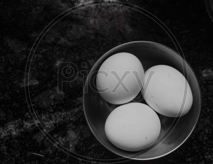 Three chicken eggs in single bowl on marble tiled floor. Selective focus on eggs. black background.