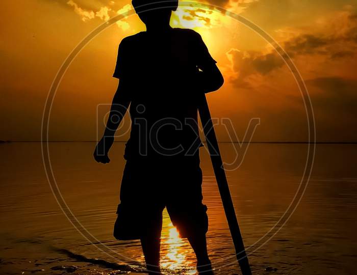 Silhouette of a boy standing near the river during sunset time.