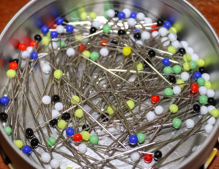 Close Up View On Lots Of Sewing Pins With Colored Heads In A Metal Box On A Wooden Table