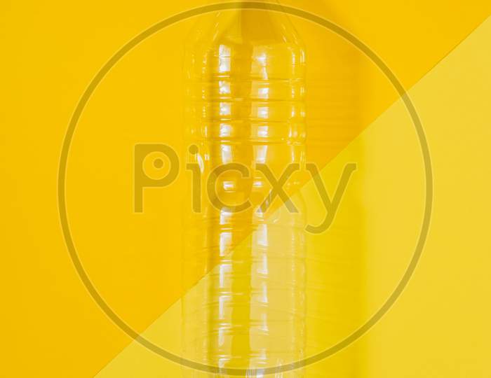 Clear Plastic Bottle With Blue Cap On A Yellow Background. Recycling And Environment Concept.