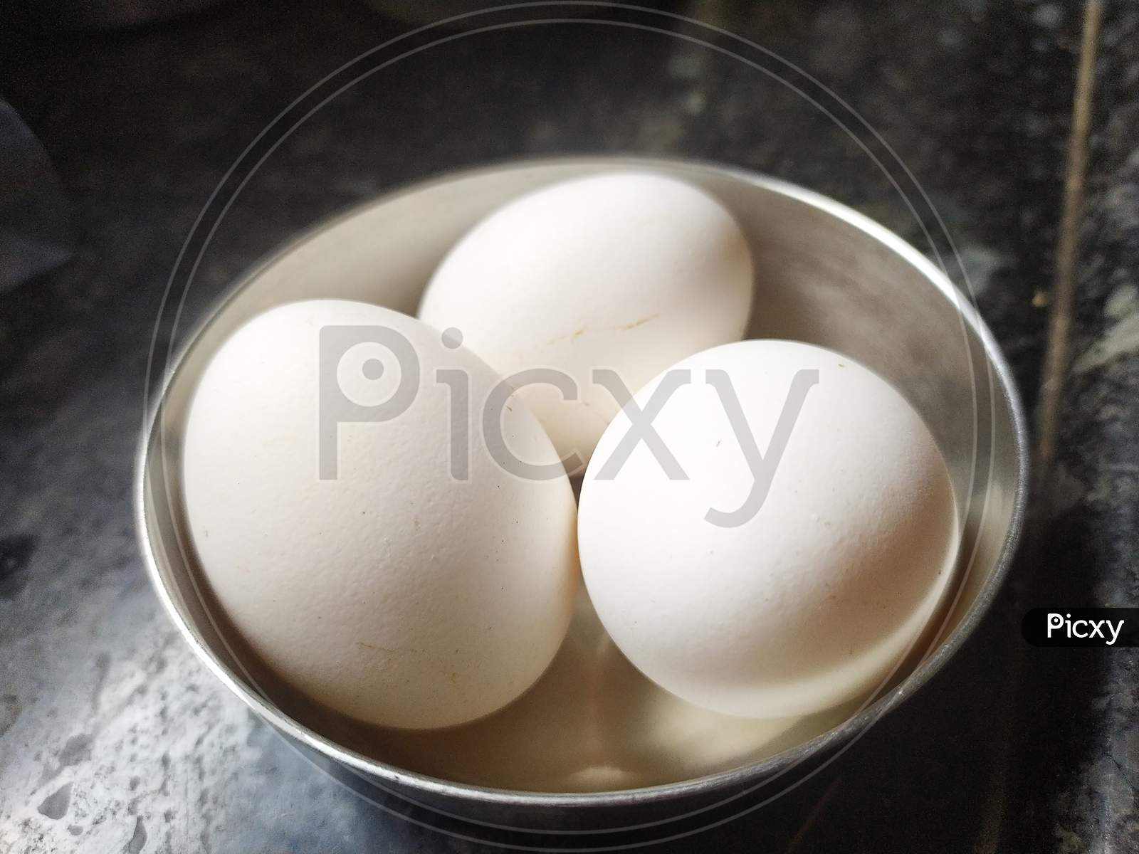 Three chicken eggs in single bowl on tiled floor.