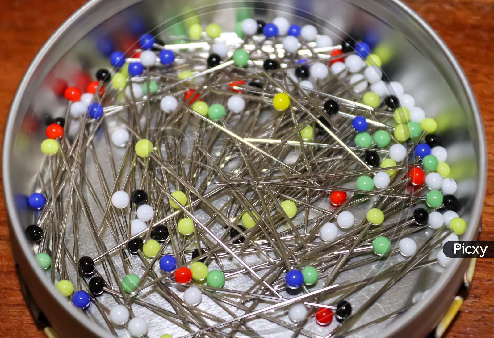 Close Up View On Lots Of Sewing Pins With Colored Heads In A Metal Box On A Wooden Table