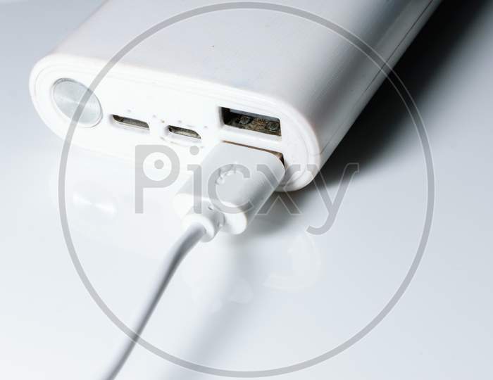 A White Power Bank With Usb Ports And Power Button. A Cable Is Attached To One Of Its Ports