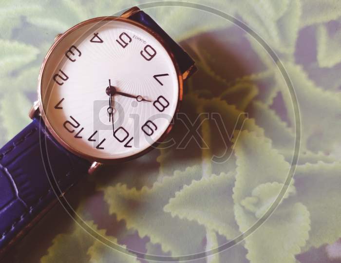 A wrist watch on the leaf textured glass floor of table.