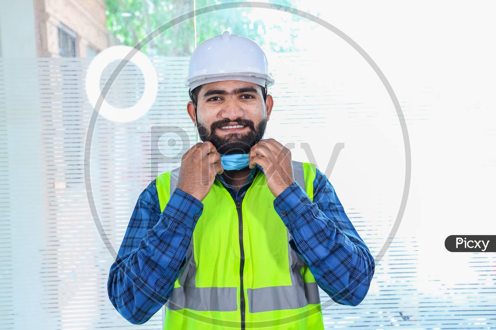 Young Engineer Taking Off Mask Smiling, Closeup Of Beard Man Wearing Blue Shirt With Yellow Vest And White Helmet, Back To Work After Lockdown Ends Due To Covid-19 Pandemic, New Normal