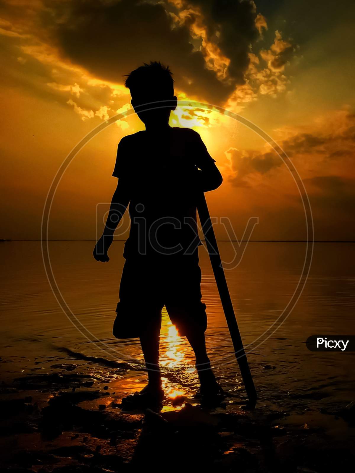 Silhouette of a boy standing near the river during sunset time.