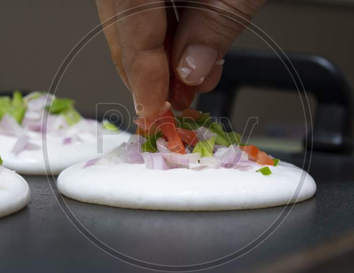 Adding Sliced Tomatoes And Capsicum On Round Utappa South Indian Dish With Fingers