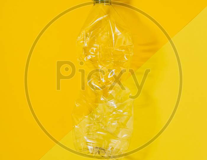 Transparent And Crushed Plastic Bottle With Blue Cap On A Yellow Background. Recycling And Environment Concept.