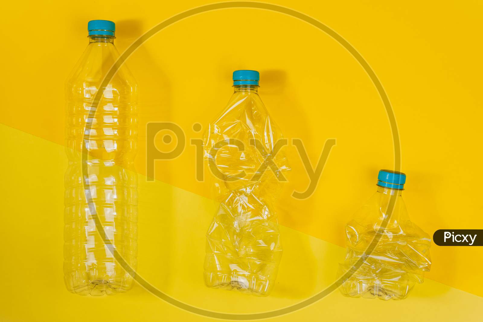 Transparent And Crushed Plastic Bottles With Blue Caps On A Yellow Background. Recycling And Environment Concept.
