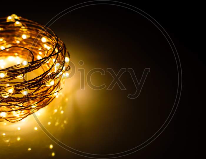 Yellow Colored Light Chain For Decoration Placed On A Reflective Surface. Space For Text In The Right