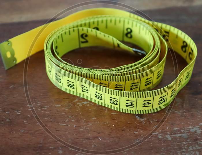 Sewing Concept. Yellow Tape Measure Isolated On A Brown Wooden Background.