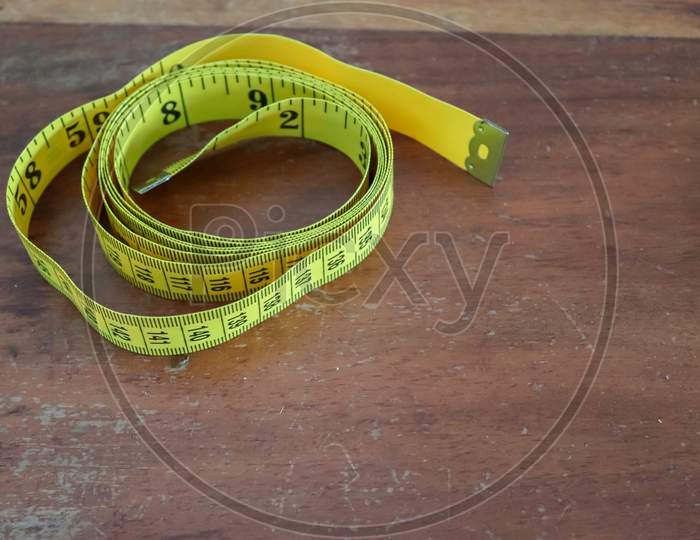 Sewing Concept. Yellow Tape Measure Isolated On A Brown Wooden Background.