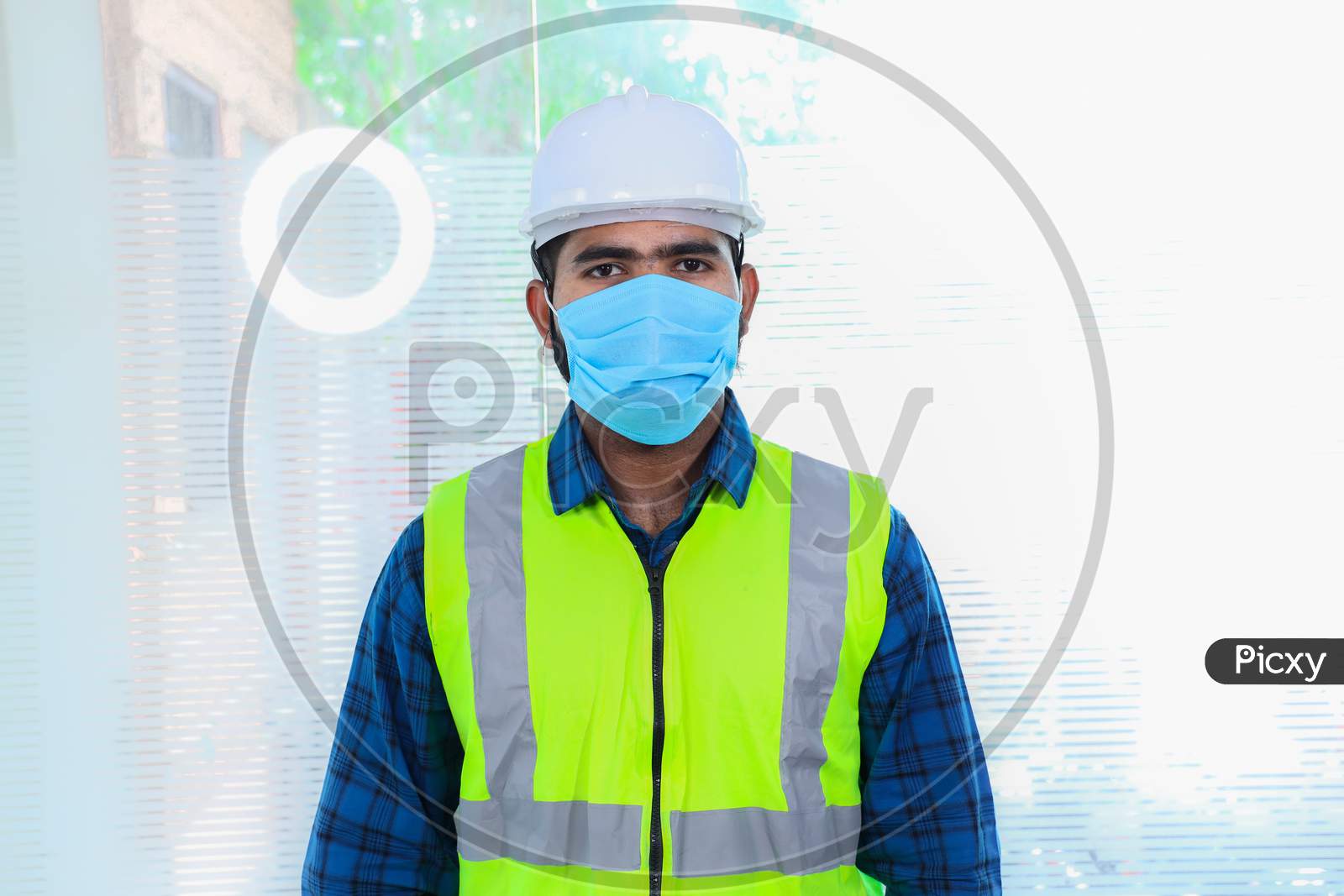 Young Engineer Wearing Mask, Closeup Of Beard Man Wearing Blue Shirt With Yellow Vest And Ywhite Helmet, Back To Work After Lockdown Ends Due To Covid-19 Pandemic, New Normal Lifestyle