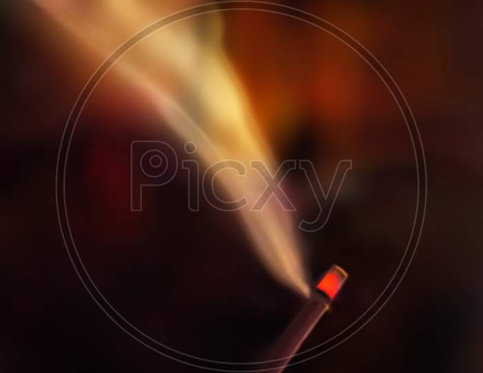 Incense burning with smoke at night. Dark background. Selective focus on red head of incense or agarbatti.