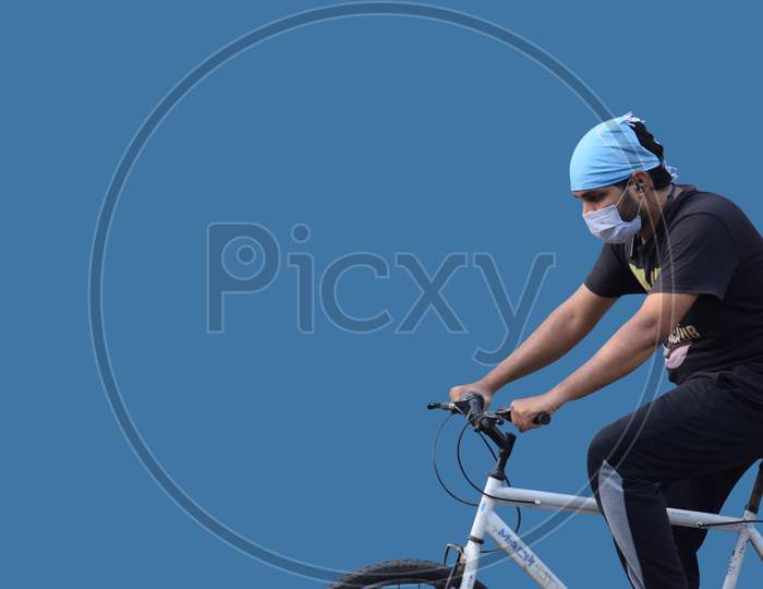 Hyderabad, Telangana, India. June-29-2020: Man With Protective Safety Mask On His Face Riding A Bicycle, Isolated On Blue Background