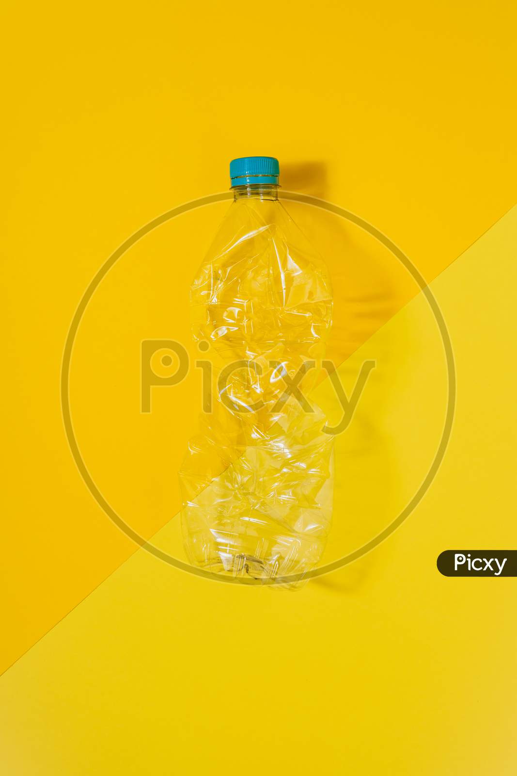 Transparent And Crushed Plastic Bottle With Blue Cap On A Yellow Background. Recycling And Environment Concept.
