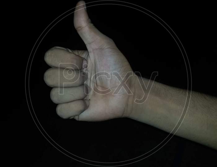 Man`s hand clenched into a fist with thumb up on the black background like gesture.