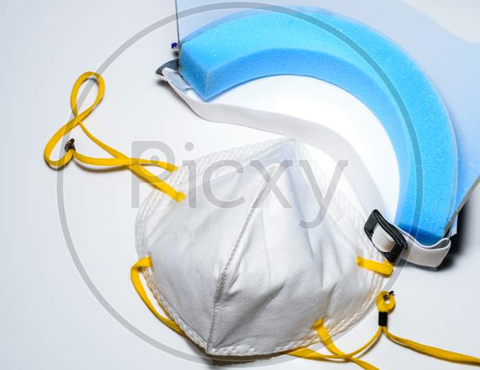 A Face Mask And A Face Shield Placed On A White Surface. To Use For Personal Protection Against Covid 19