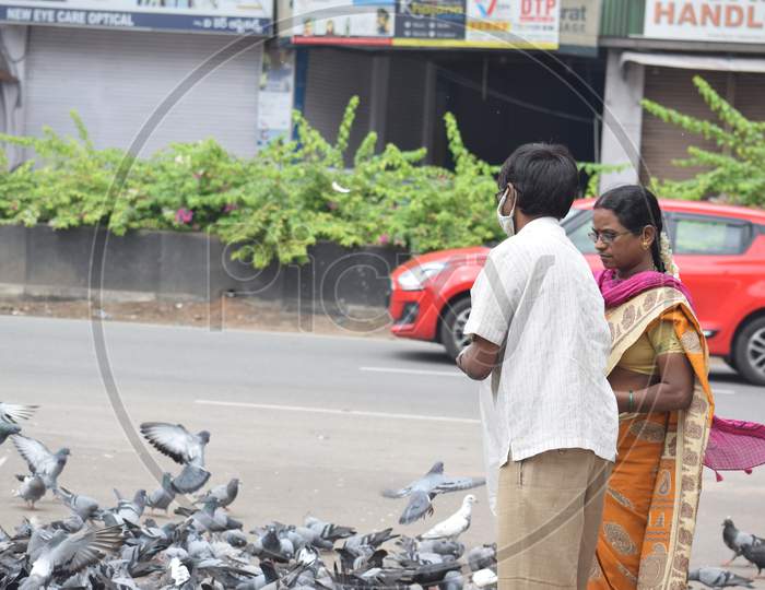 Hyderabad, Telangana, India. july-13-2020: A man and woman is feeding pigeons all around at street road in corona virus pandemic time, peoples caring on birds, wearing mask,  pigeons on road side