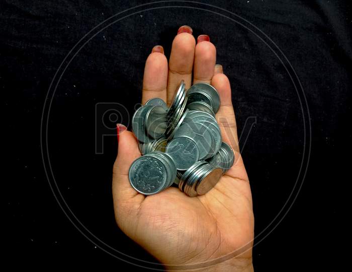 a hand holding lots of silver coins in black background with some selective focus