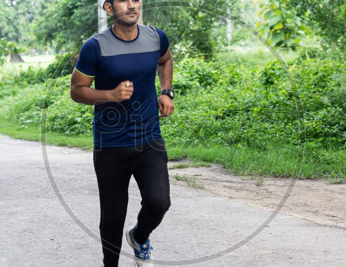 Asian Runner  wearing sportswear jogging outdoors with tree's in background. Male sports and fitness concept.
