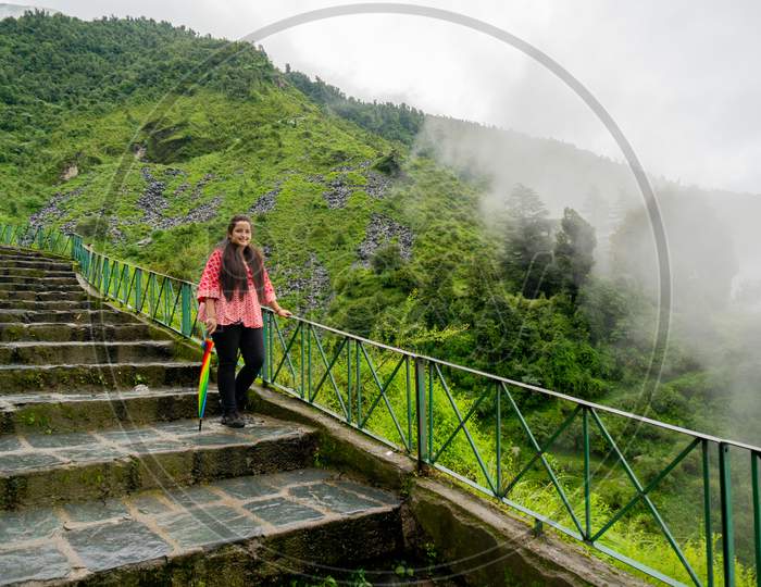 Young Indian Girl In A Red Dress Standing On A Series Of Stairs Leading To The Bhagsu Falls In Mcleodganj In Himachal India