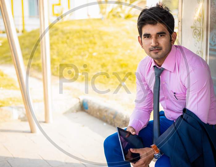 Young businessman or entrepreneur waiting at bus stop with his tablet or mini laptop or ipod