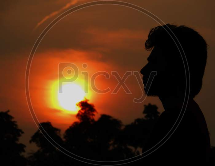 silhouette young men standing at sunset, side view, orange sky with silhouetted trees