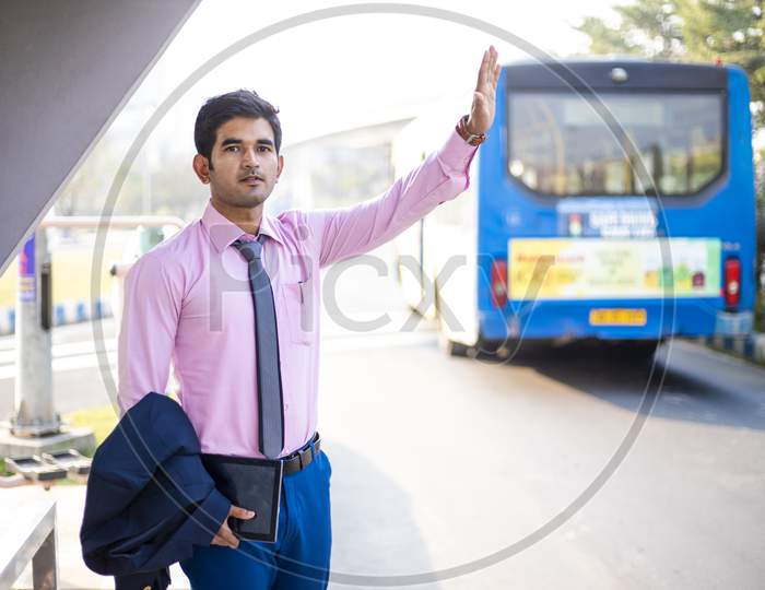 Young Asian businessman in formal dress standing at bus stop and waving his hand for Taxi or Bus