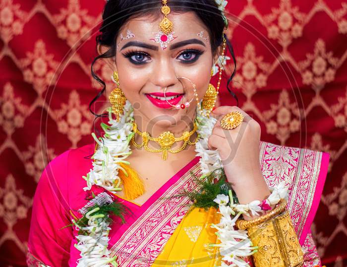 Stunning Indian bride dressed in Hindu red traditional wedding clothes sari embroidered with gold jewelry and a veil smiles tender