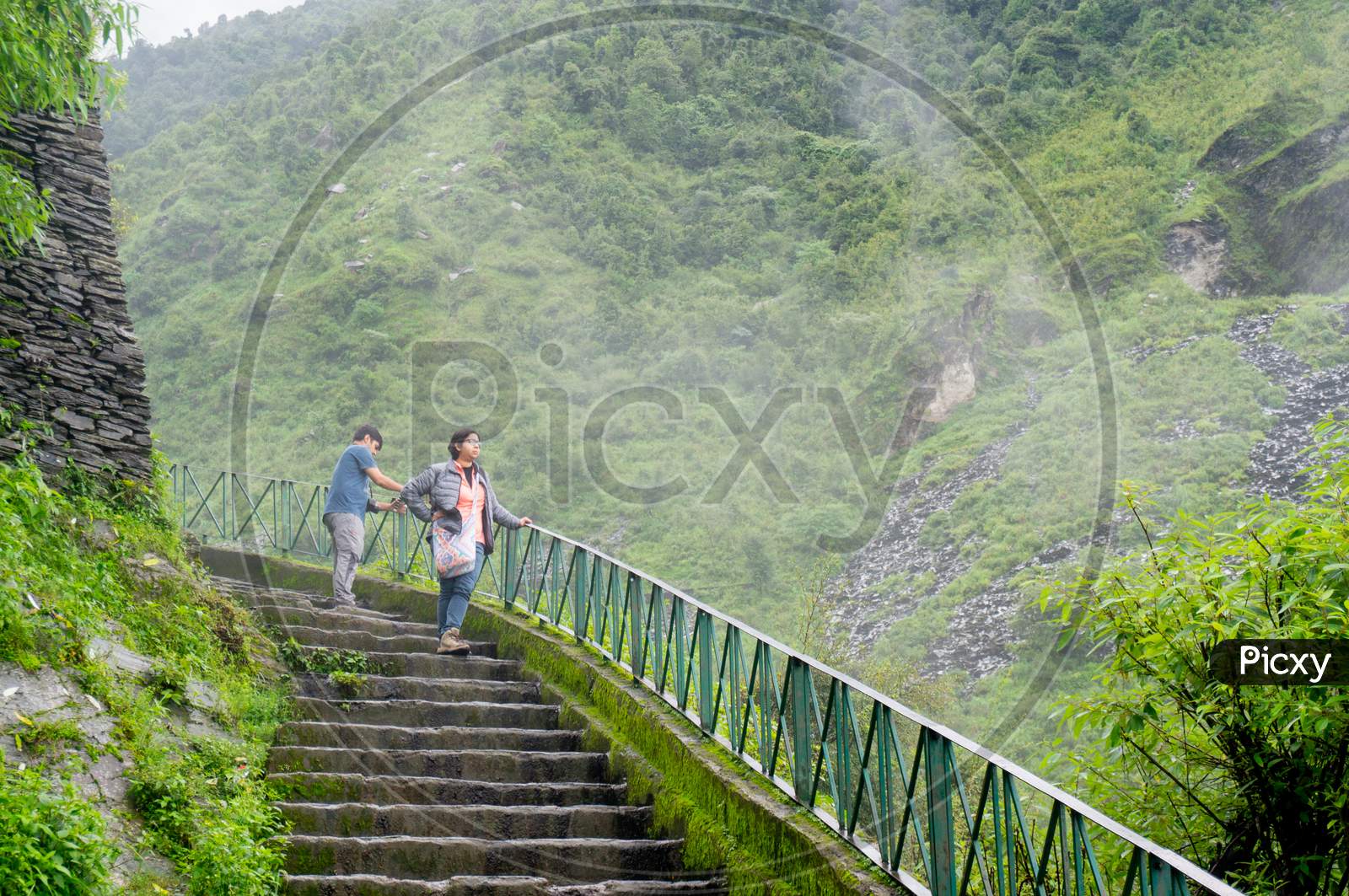 Couple Standing On A Series Of Steps With Clouds Mist And Fog On The Beautiful Green Hills Of Triund Trek In Mcleodganj Himachal Pradesh